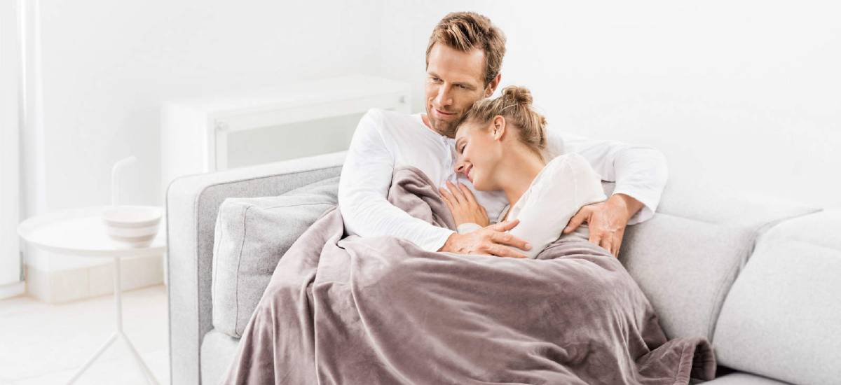 Vyras ir moteris meiliai susiglaudę apsikloję švelniu pledu