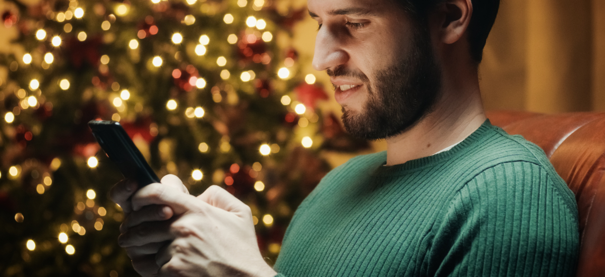 Vyras Kalėdinių lempučių fone naršo telefone